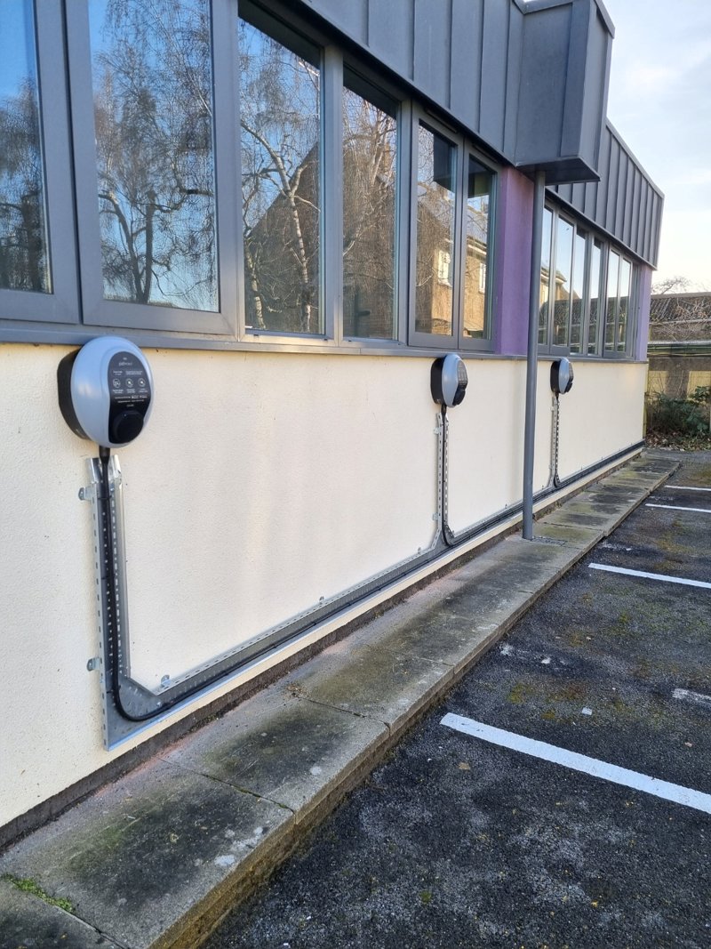 Three wall-mounted EV chargers on a commercial building car park